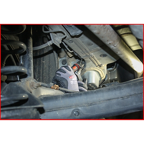 Nahaufnahme von jemandem, der unter einem Auto arbeitet. Eine Hand in einem grauen Handschuh hält ein Werkzeug.